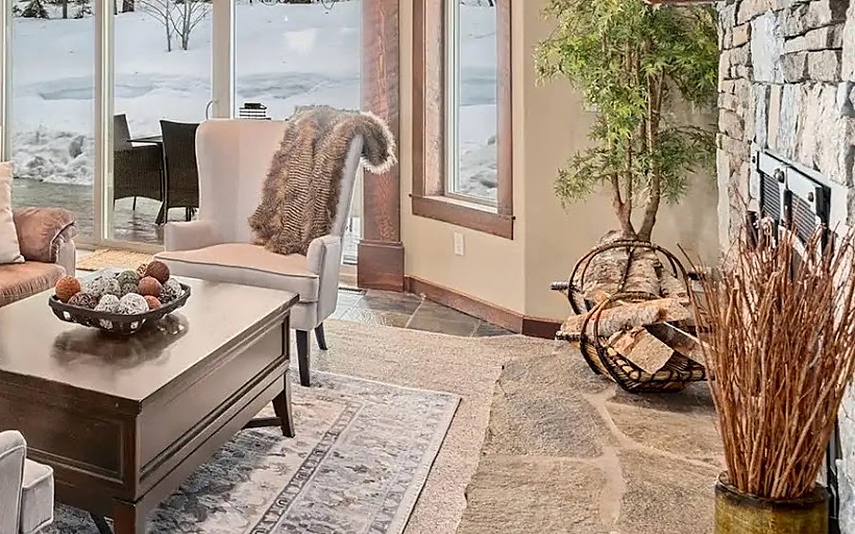 Cozy seating nook beside a stone fireplace with a faux fur throw and snow-covered view